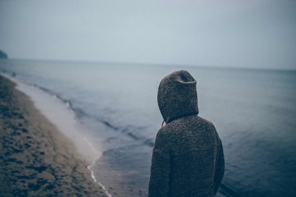 person wearing a dark hoody looking out onto a beach