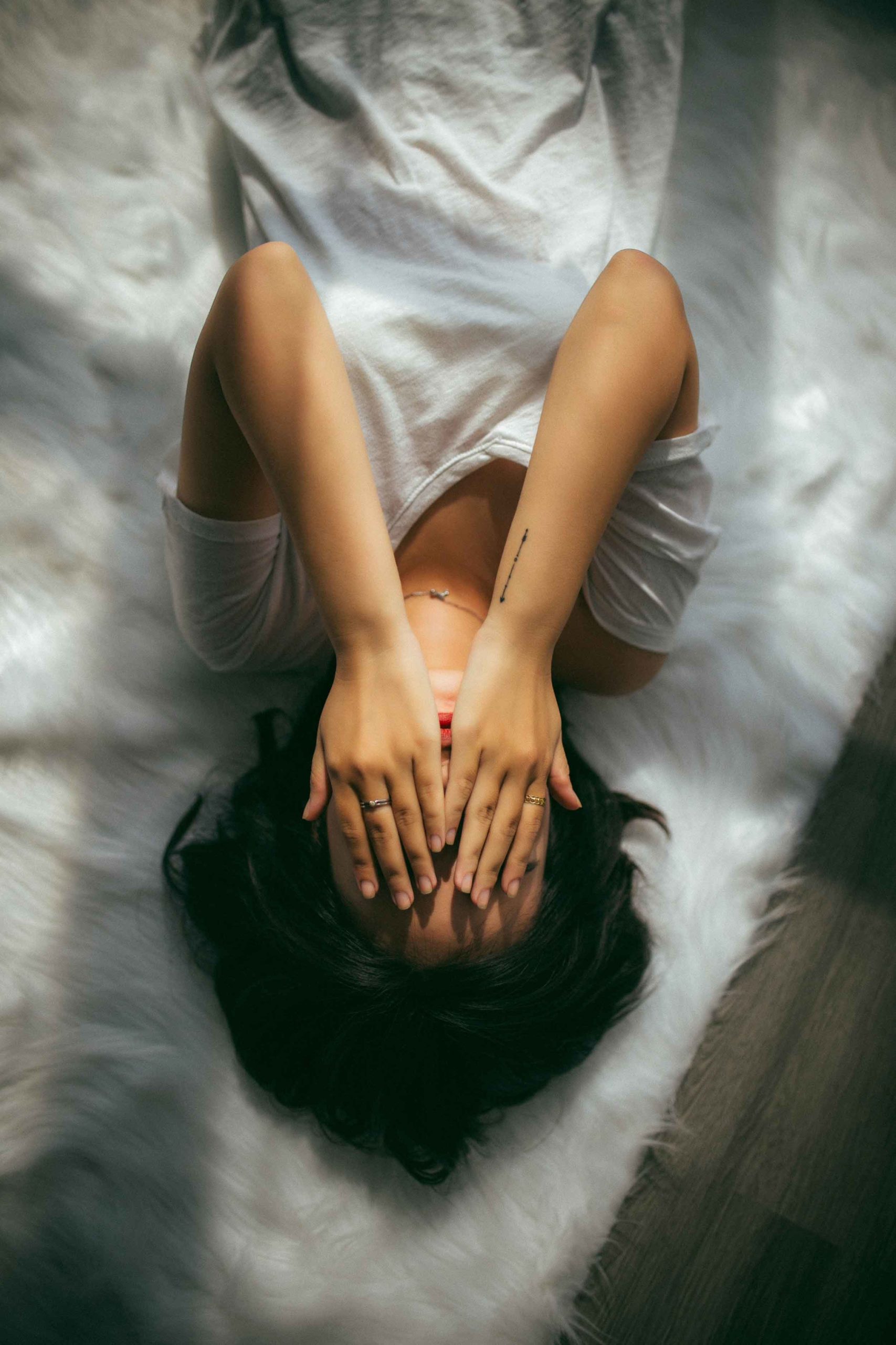 young woman laying on a bed with her hands covering her face