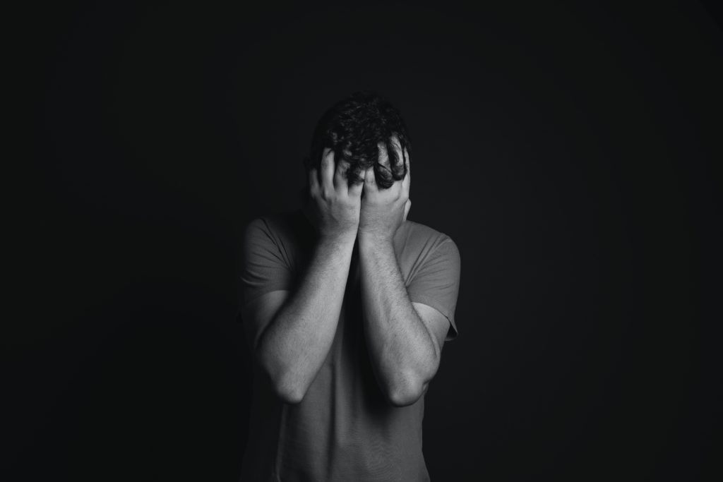 grayscale photo of a young man with his hands covering his face