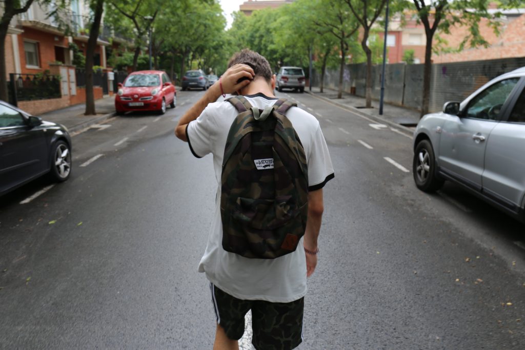 teenager walking down the street with head down wearing backpack