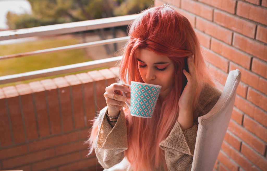 young lady with pink hair sipping coffee on an outdoor balcony