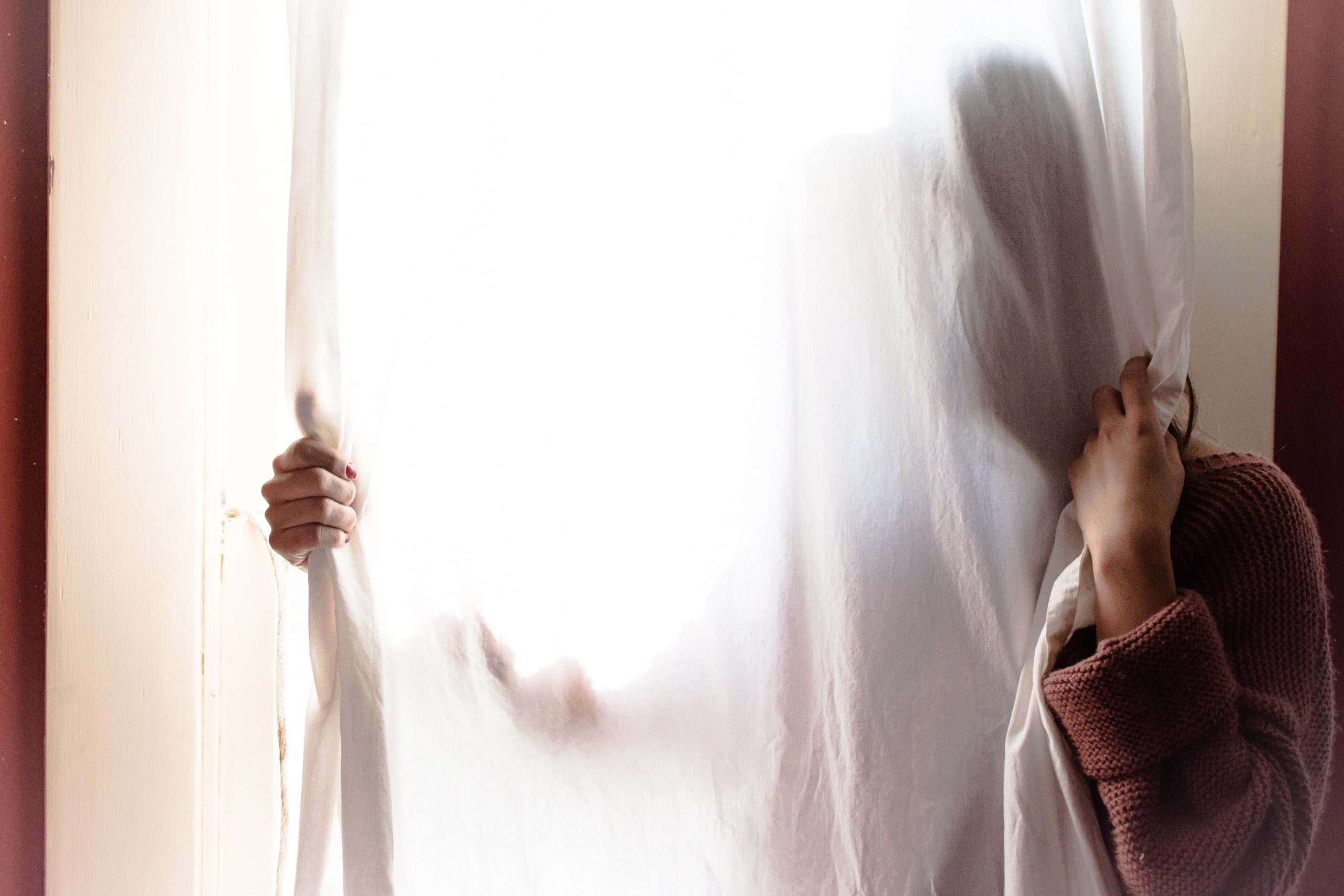 woman standing behind a sheer curtain hiding her face